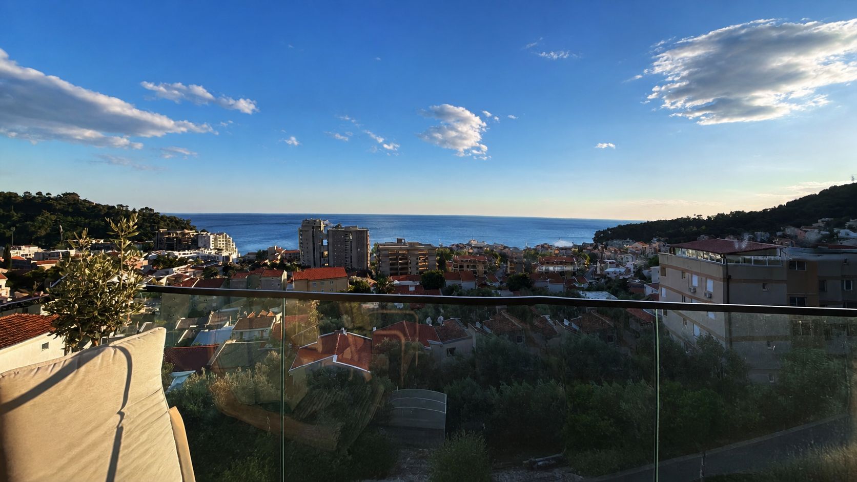 View from the apartment terrace across the glass railing and Petrovac rooftops towards the Adriatic under a blue sky
